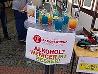 Ein Informationsstand mit bunten Getränken und einem Banner mit der Aufschrift "Alkohol? Weniger ist besser!"